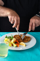 male hand eating from big dish German schnitzel with salad