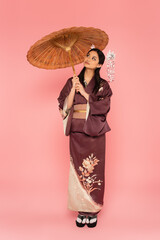 Young japanese woman holding umbrella on pink background