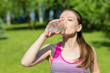 young caucasian woman athlete drinking water on workout outdoor. girl is thirsty doing sports on hot summer day. healthy lifestyle concept.