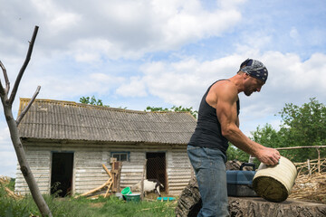 Side view of muscular farmer in bandana holding bucket on ranch 