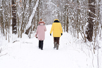 Fototapeta na wymiar A woman with a teenage child in bright jackets are walking in a winter snow-covered forest. People, lifestyle concept