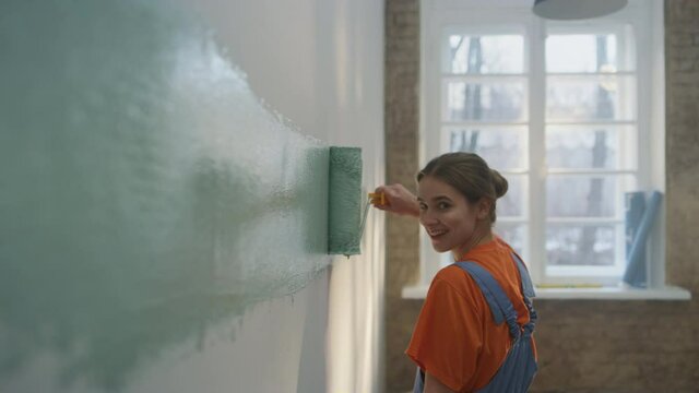 Happy woman doing home repair indoors. Girl making wide strip of paint on wall.