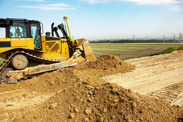 Asphalt road construction process. The bulldozer levels and compacts the clay soil for the base of the highway. Earthworks on a summer day.