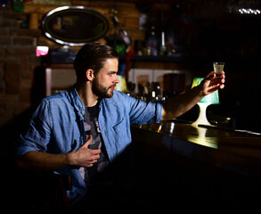 Macho holds glass of shot or liqueur in bar.