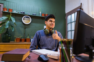 teenage boy sitting at his desk having a virtual class, wearing a gray sweater, being happy