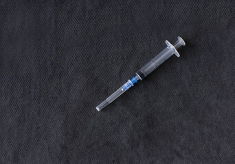 a disassembled medical syringe for injection with a metal needle lies on a dark gray fabric background