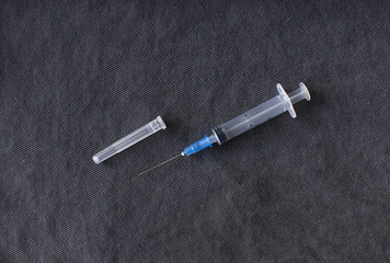 a disassembled medical syringe for injection with a metal needle lies on a dark gray fabric background