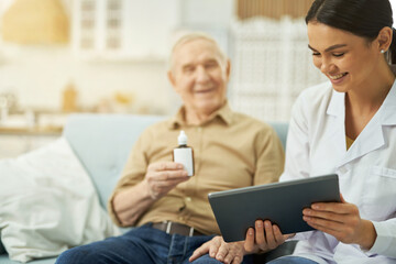 Female doctor and senior citizen looking at tablet screen at home