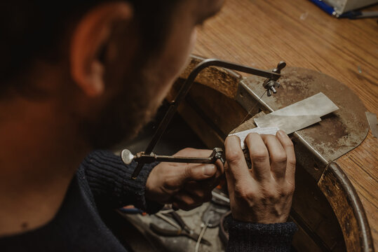 Crop jeweler sawing metal on workbench