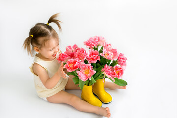 Obraz na płótnie Canvas A little girl laughs loudly and touches pink tulips standing in rubber boots instead of a vase. Holiday card with tulips and a child on a white background with a place for text