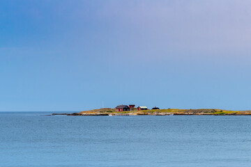 Fototapeta premium small red cottages on an isthmus of land in the middle of a calm ocean under a blue sky