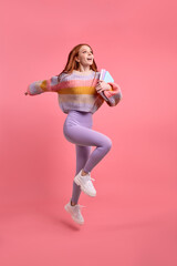 Full body profile photo of pretty redhead female student jump high holding notebook in hands hurry in university, in casual outfit isolated over pink color background. Portrait