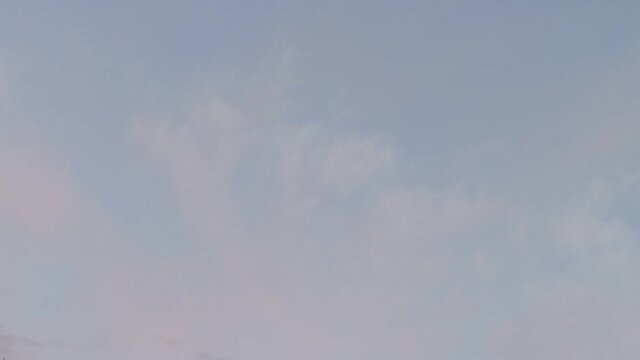 Light gray clouds fly across the sky. Summer evening across the blue sky from bottom to top, gray-pink clouds float in a continuous layer, gray clouds appear from below.