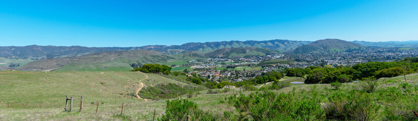 Fototapeta na wymiar Elevated panoramic scenic view of San Luis Obispo urban area sprawl and green mountains of Santa Lucia Range from Bishop Peak Trail on sunny spring day