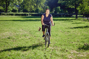 Fat woman rides bicycle in park, concept of body positivity and healthy lifestyle.