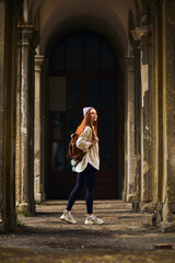 Fototapeta na wymiar Redhead Tourist female travel destination visiting abandoned old place on vacation. Beautiful woman walking on summer holidays, cold weather outdoors. Woman is dressed in coat and hat