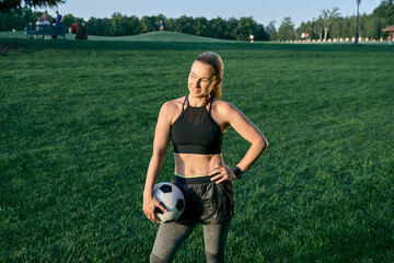 Sporty lady. Athletic beautiful middle aged woman, soccer player smiling and holding the ball while standing on the grass outdoors on a sunny day