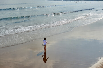 young woman in a white shirt walks along the beach of san lorenzo in Gijon