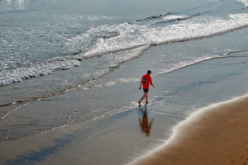 young man with orange sweater walks along the beach of san lorenzo in Gijon