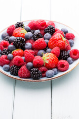 Fresh berry salad on blue dishes. Vintage wooden background.