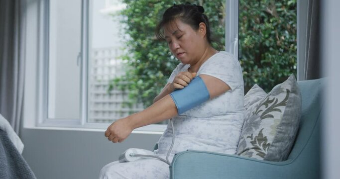 Asian woman using blood pressure monitor sitting on couch at home