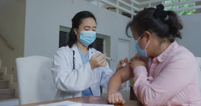 Asian female nurse wearing face mask giving covid vaccination to female patient in hospital