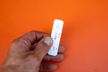 Hand with a positive test result of a covid-19 rapid test for self-application in front of an orange background.