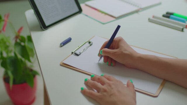 Female hands writing with pen Planes para hoy - Plans For Today in Spanish sign on sheet of paper working with tablet computer sitting at the desk.