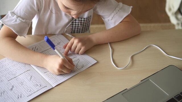 Girl make math homework at home, use textbook and laptop Spbd. Elementary school kid make exercise