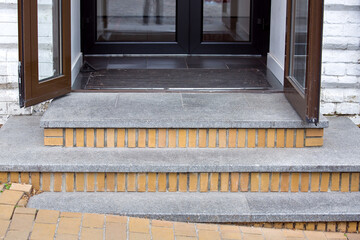 threshold with granite steps of a brick house with brown iron doors with glass and foot mat...