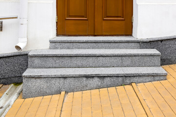 granite threshold at the entrance door made of brown wood and white facade with stone cladding of...