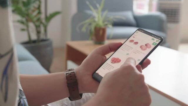 Man Sitting On Couch Using Smartphone Buys In Internet Shop. Male Selects Beef In Grocery Online Store

