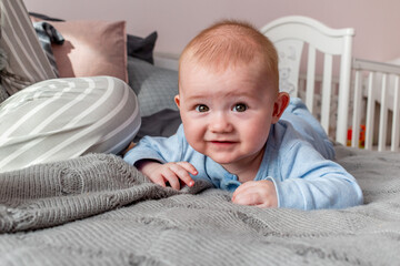 Baby looks the camera and smiles next his young mother sits on the bed.