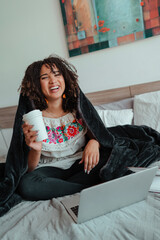 black woman sitting on her bed using a laptop with a coffe