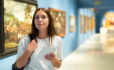 Portrait of a young girl visitor with a paper guide at the exhibition of paintings in the museum..
