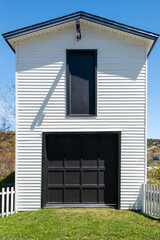 A tall double story white wooden clapboard siding building with a vintage wooden black garage door....
