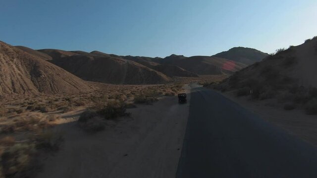 Following an off-road vehicle four-wheel drive along the dusty edges of a paved road in the Mojave Desert - aerial first person view