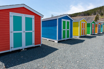 Fototapeta na wymiar Multiple wooden sheds with colorful double doors. The buildings are blue, yellow and green storage buildings. The colorful huts have white trim on the edges. The background is a blue sky with clouds. 