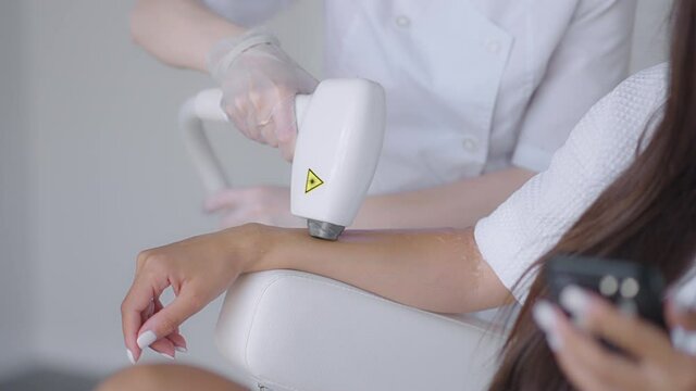 Procedure of removing hairs on hand. Laser hair removal on a diode laser, tracking moving camera. Woman cosmetologist applies laser hair removal gel on female hand. photoepilation, body care concept.