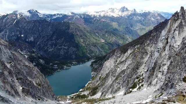 High flying drone footage of Colchuck Lake, it's turquoise water, and high above Aasgard Pass near The Enchantments in Washington's Cascade Mountain Range - Moss, trees, and snowy cliffside