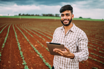 Naklejka na ściany i meble Young Latin farmer working with digital tablet on peanut plantation. Brazilian farmer looking at camera.
