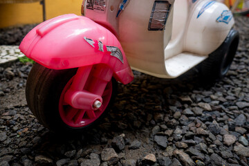 black wheels of pink toy mini scooter on black rocks