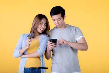  Asian couple holding credit card and smartphone isolated on yellow background