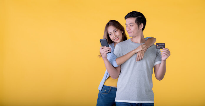 Excited Asian Couple Holding Credit Card And Smartphone Feeling Excited While Looking At A Mobile Phone Isolated On Colour Background