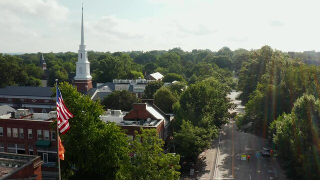 American flag flies with orange flag promoting anti gun, shooting, violence. Suicide homicide prevention awareness by protesters. Church steeple in small town. Automatic rifle and assault weapon ban.