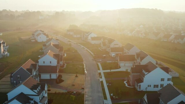 New residential housing development in USA at sunrise. Neighborhood community. Reverse revealing aerial at sunrise with moody beautiful fog scene.