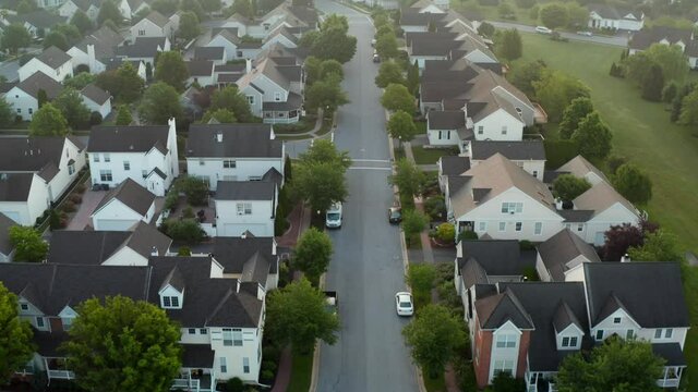 Suburban homes in residential American suburbia. Houses along street in summer aerial drone shot. USA population growth theme.