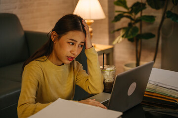 Frustrated young Asian female entrepreneur with hands on head feeling irritated, tired and tensed...
