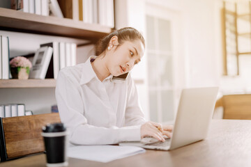 Pretty businesswoman sitting on the phone at her desk with laptop computer and notepad in hustle...