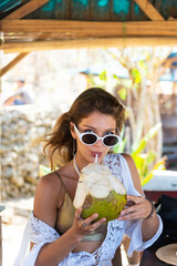 Happy pretty  young woman holding fresh cocnut cocktail when standing on beach